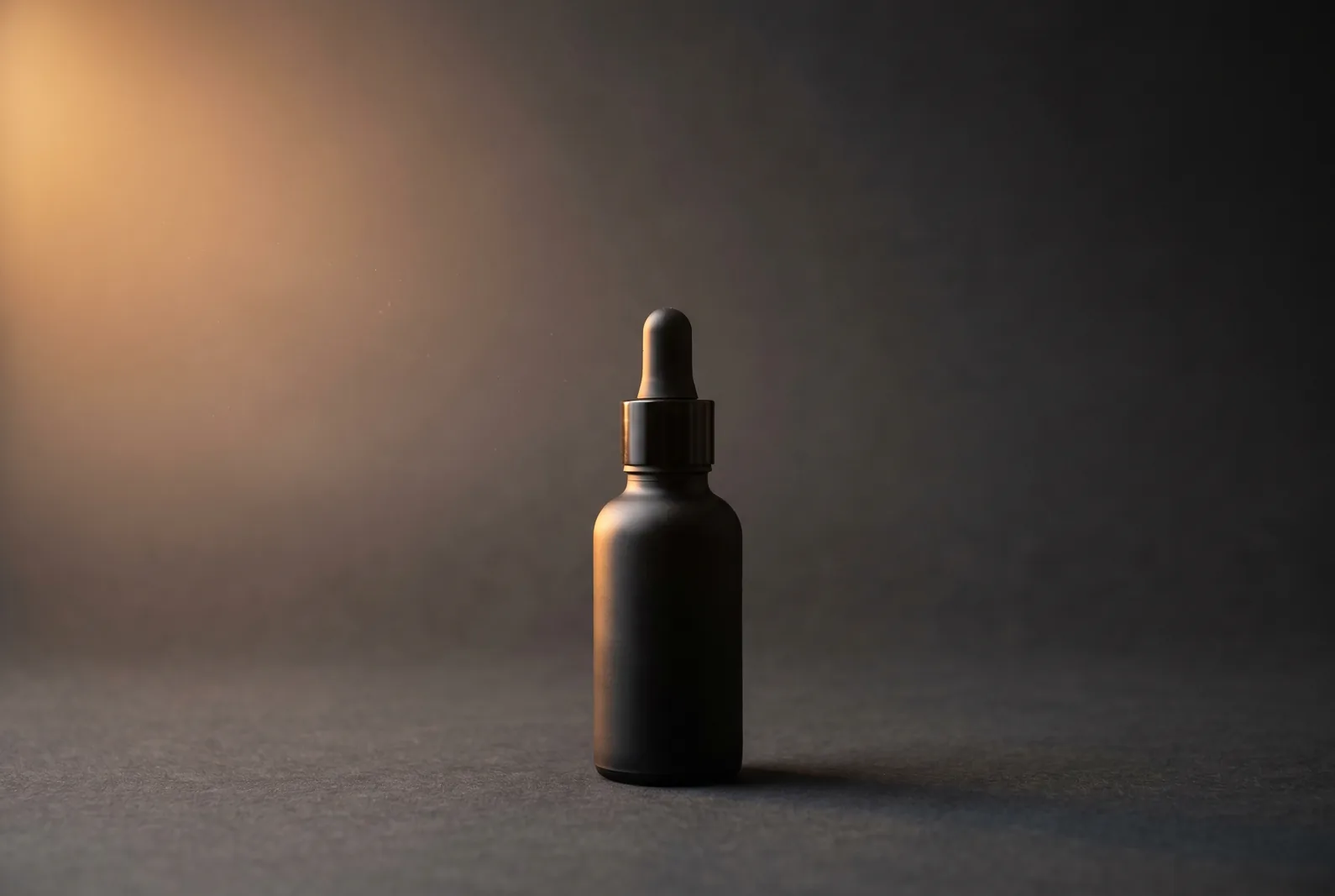 Hero-Packshot einer mattschwarzen Tropfflasche mit warmem Amber-Licht auf dunklem Hintergrund.